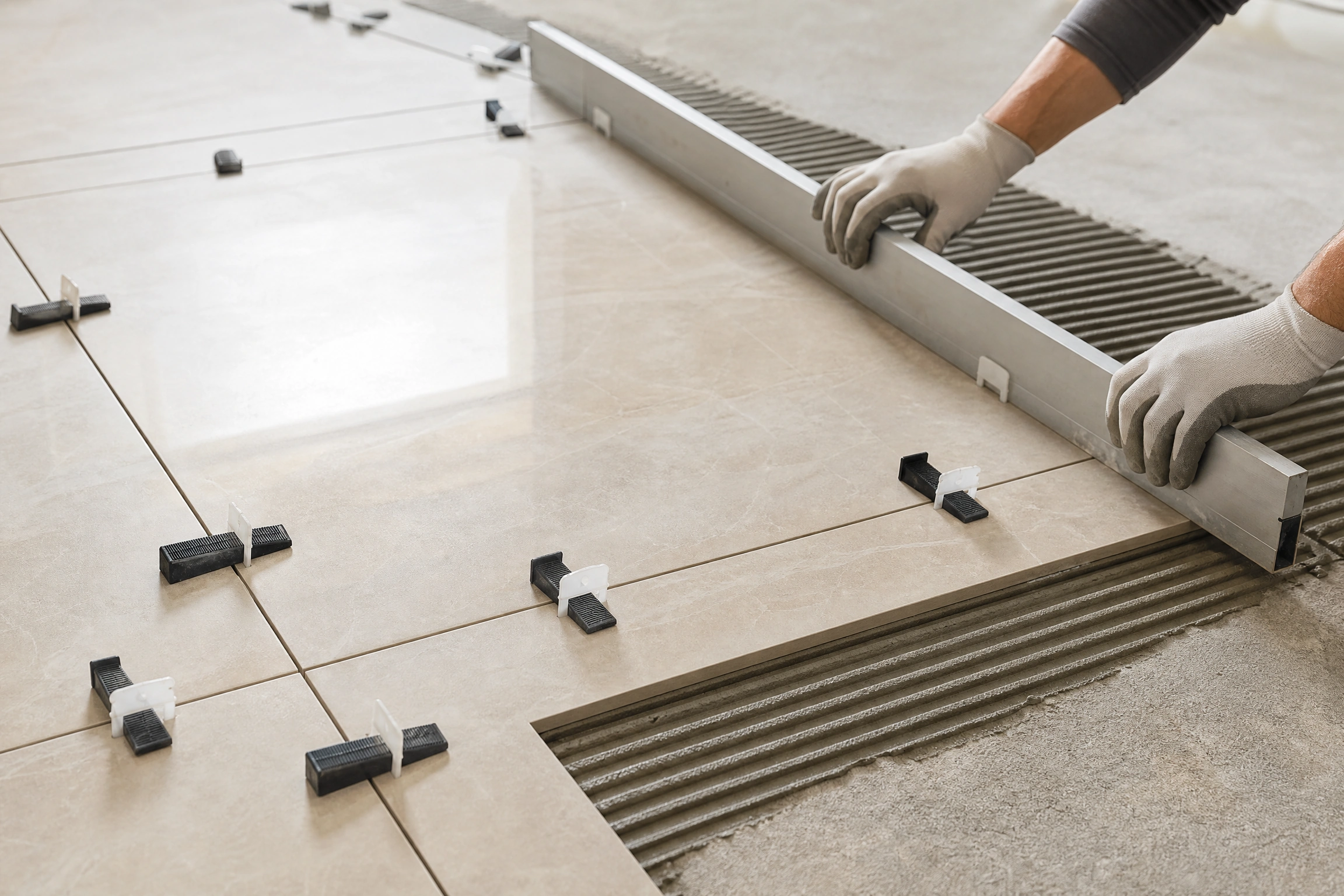 Professional installer positioning a large-format porcelain floor tile with alignment clips